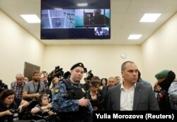 Alexei Navalny y Daniel Kholodny, director técnico de su canal de YouTube, aparecen en una pantalla de TV desde prisión durante una audiencia este martes en el tribunal de apelaciones en Moscú. (REUTERS/Yulia Morozova)