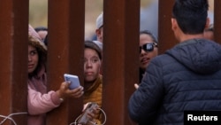 Migrantes se acercan a la valla fronteriza para intentar cargar sus teléfonos en la frontera sur de EEUU. Foto: Reuters.