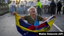 Consuelo Márquez sostiene una bandera venezolana frente a la policía que bloquea manifestaciones contra los resultados oficiales de las elecciones en Venezuela. (AP/Matías Delacroix)