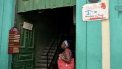 Una mujer parada junto a dos señales de negocios privados en Cuba. / AFP PHOTO / YAMIL LAGE