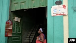 Una mujer parada junto a dos señales de negocios privados en Cuba. 