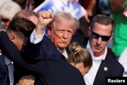 El expresidente Donald Trump levanta el puño mientras es asistido por el Servicio Secreto después de que se escucharan disparos durante un mitin de campaña en Butler, Pensilvania, el 13 de julio de 2024. REUTERS/Brendan McDermid